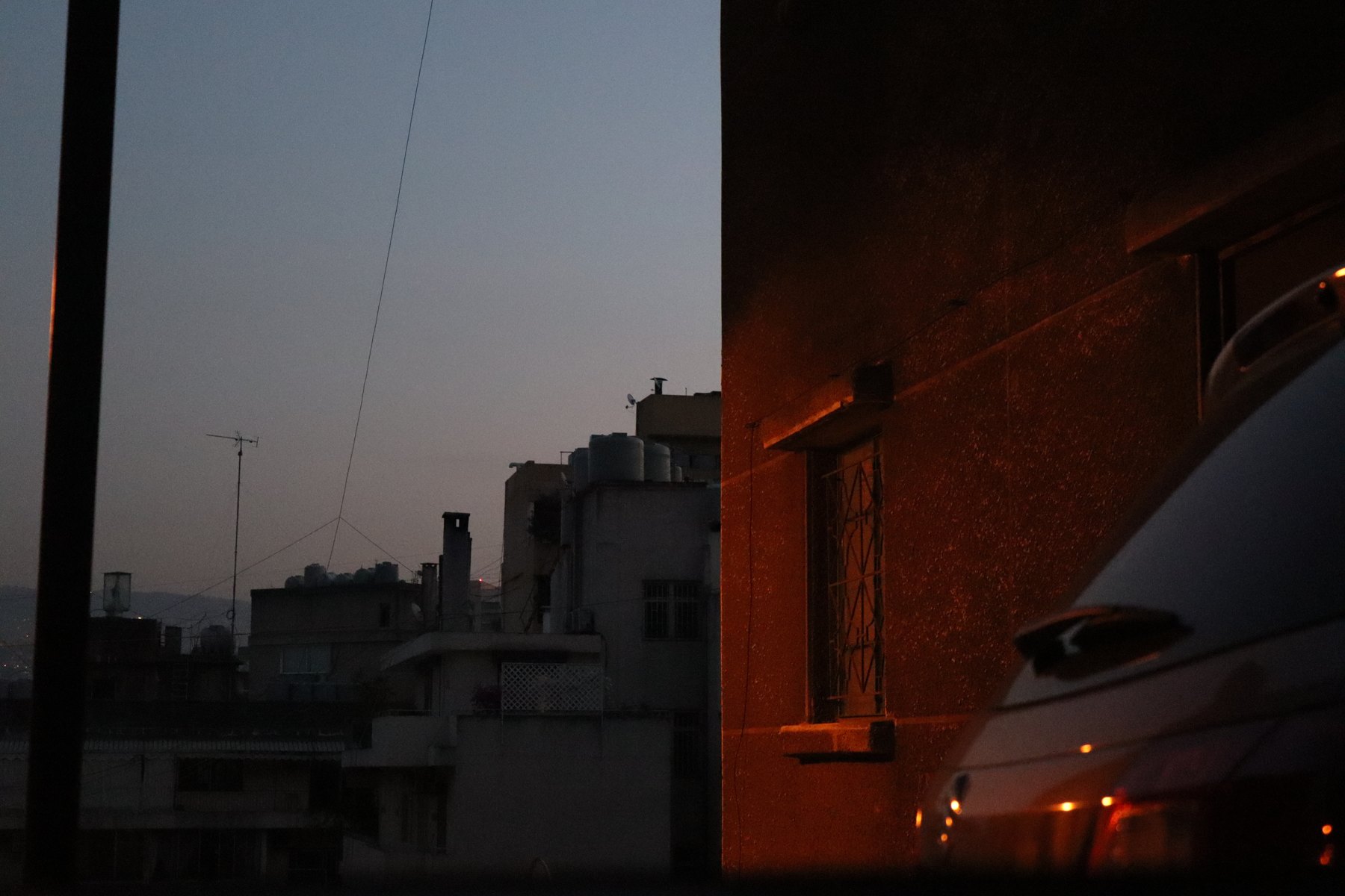 Rooftops at dusk beside a wall lit orange by a single lamp