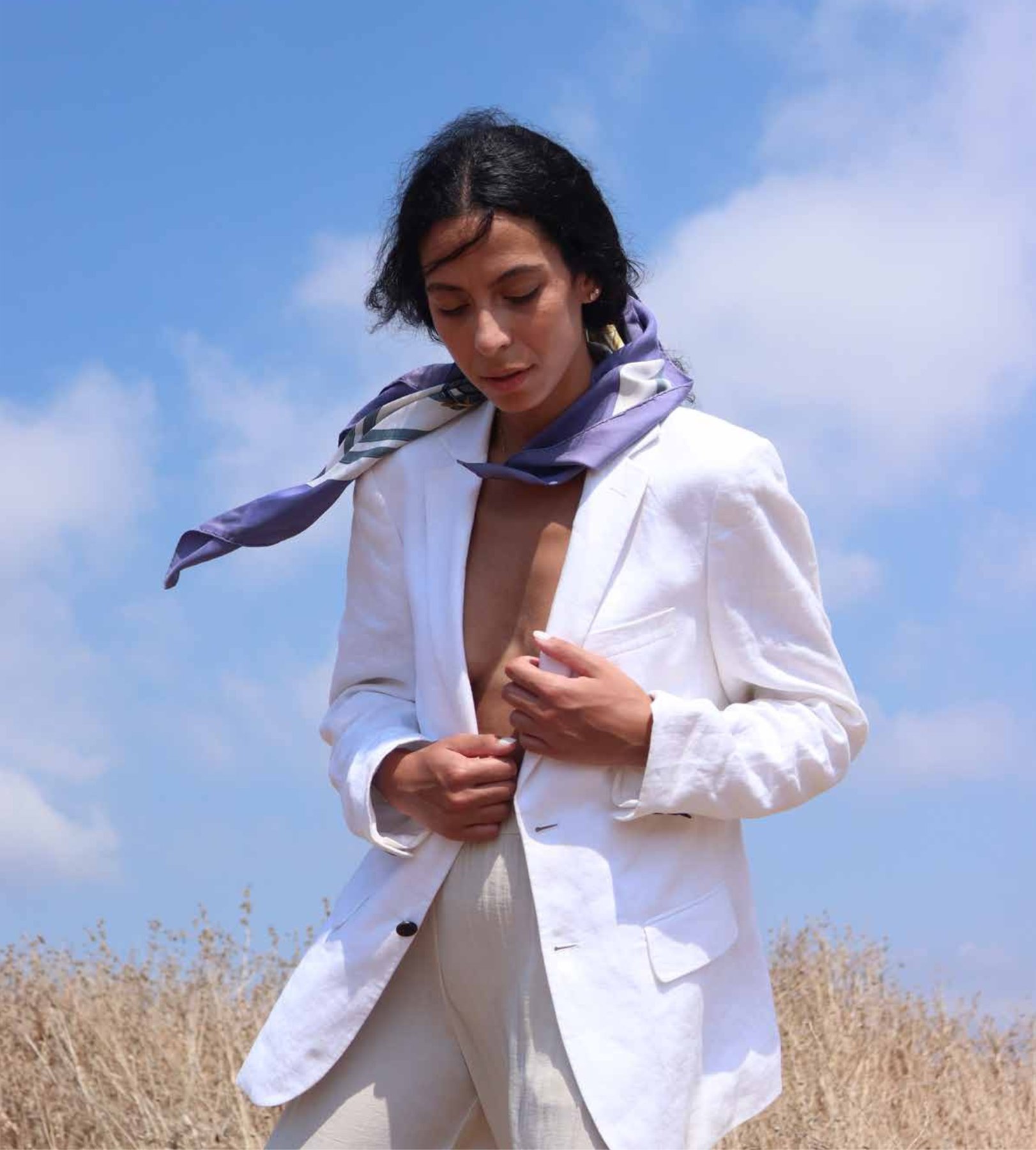 Woman in a white blazer and lilac scarf against a blue sky