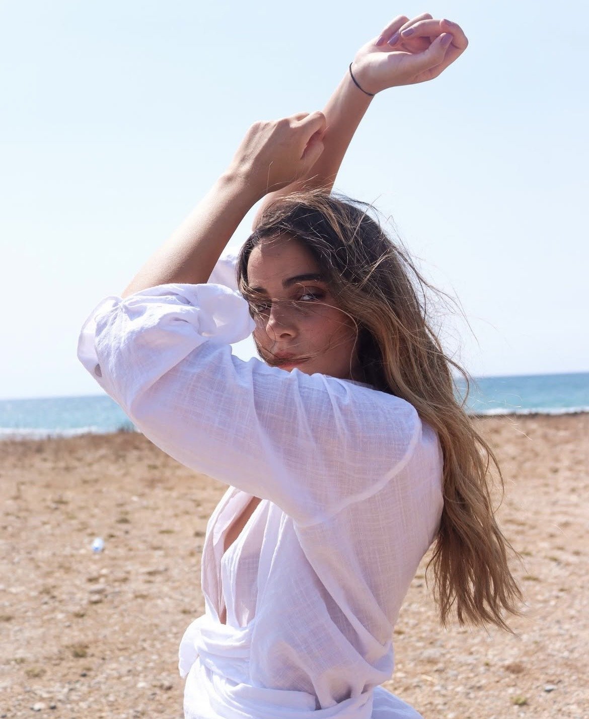 Woman by the sea, arms raised, hair across her face
