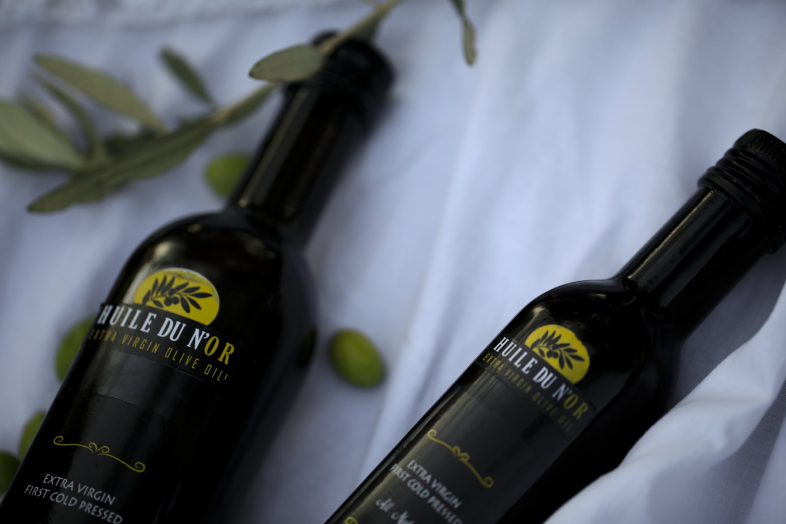 Two Huile du N’or bottles on white linen with olive branches