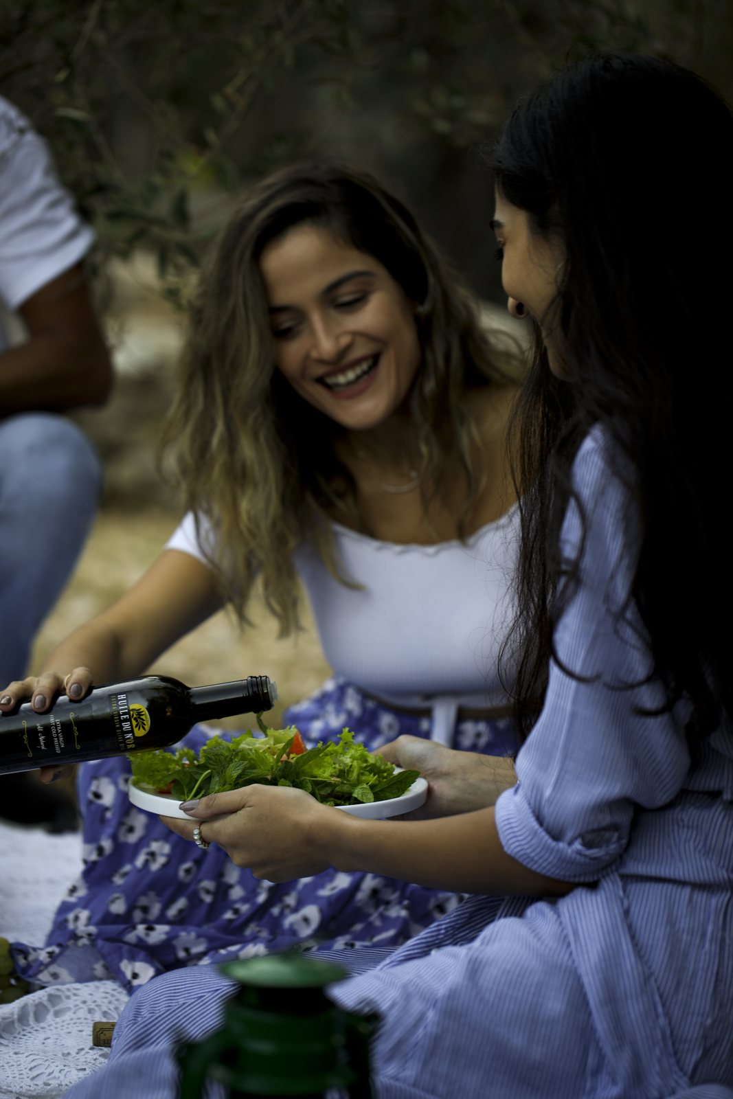 Friends at a picnic pouring olive oil on a salad
